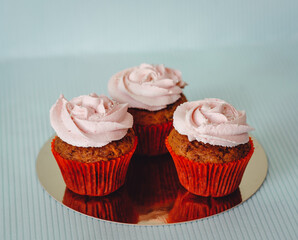 three carrot cupcakes on a blue background with a pink cream