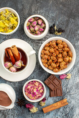a cup of herbal tea with different dry flowers and chocolate and a bowl of nut on grey ground