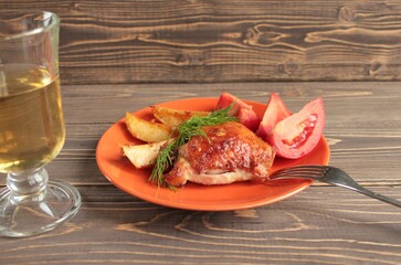Chicken, potatoes and tomatoes are laid on a platter on a wooden surface.
