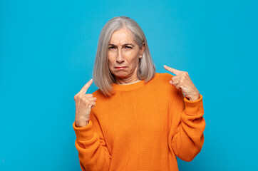 middle age woman with a bad attitude looking proud and aggressive, pointing upwards or making fun...