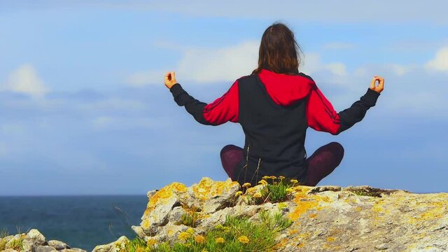 mujer joven haciendo yoga mirando al mar encima de una roca con musgo amarillo 