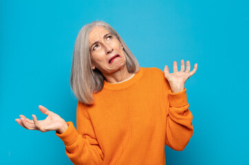 middle age woman shrugging with a dumb, crazy, confused, puzzled expression, feeling annoyed and...
