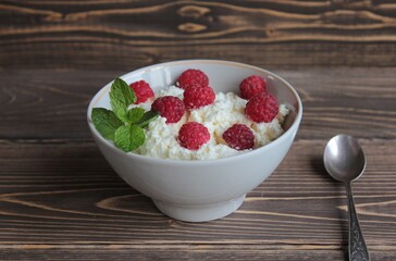 Cottage cheese with raspberries lies in a bowl on a wooden surface.   