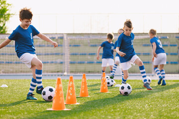 Young footballer improving dribbling skills on turf football training pitch. Kids in sportswear...