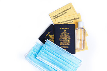 Two Canadian passports with yellow immunity vaccination records, face sanitary blue masks and sanitiser. Safety measures against coronavirus covid-19 spread. Mandatory vaccine for traveling.
