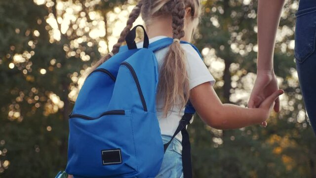 mom and daughter go to school. happy family education concept. schoolgirl with mom and daughter go hand in hand to school on footpath in the park. little lifestyle girl with a briefcase time to study