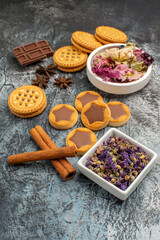 sidewise view of cookies on wooden platter and chocolates and bowls of dry flowers on grey ground