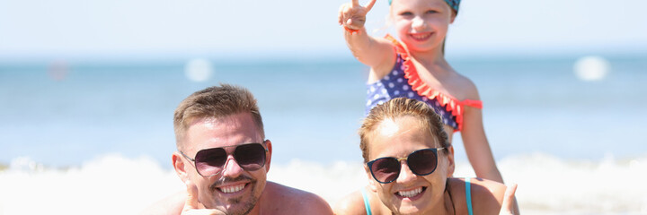 The family lies on seashore and holds thumb up. Family tour and travel concept