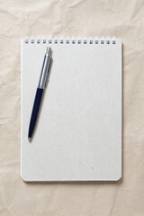  Gray notepad with white coiled spring and pen on a background of beige crumpled craft paper