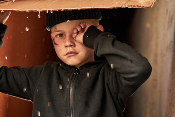 homeless child use cardboard so as not to get wet, while raining outdoors, he is crying