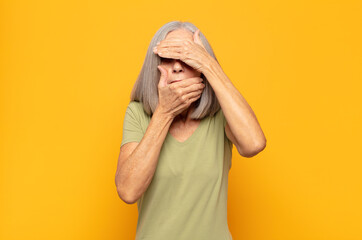 middle age woman covering face with both hands saying no to the camera! refusing pictures or...