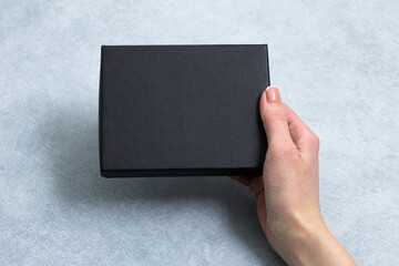 Mockup. Template. Female hand holding black box on gray textured background