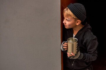 lonely street boy begging, hiding behind builsing wall, poor and hungry boy in dirty wear
