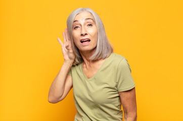 middle age woman looking serious and curious, listening, trying to hear a secret conversation or...