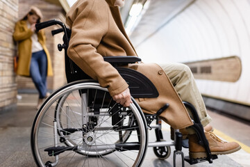 Obraz premium side view of elderly disabled man on metro platform, and woman on blurred background