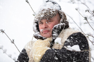 A frozen man wraps himself up in winter clothes in winter. A man in a fur hat in cold weather.