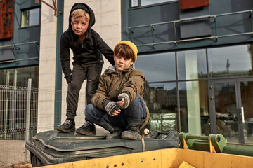two homeless orphans sit on public trash can outdoors, try to find some meal, food. crisis,...
