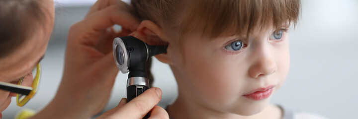 Otorhinolaryngologist examines little girl's ear with otoscope. Adenoiditis as cause of otitis...