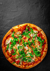 Pizza with chicken, bacon, cheese, tomato and arugula. Italian pizza on Dark grey black slate background