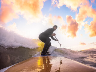 Obraz premium Adventurous Man Surfing the waves at the Pacific Ocean in Tofino, Vancouver Island, British Columbia, Canada. Dramatic Colorful Sunset Sky. Extreme sport