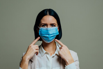 Portrait of a  young woman pointing at her face mask  to indicate everyone must cover nose and...