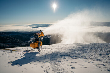 Snow cannon prepares ski slope early in the morning. Yellow snow blower machines used for preparing...