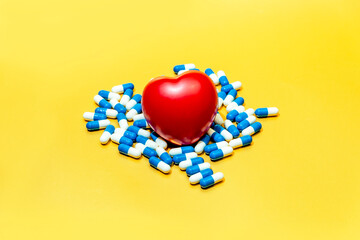 red toy heart among medicinal capsules lies on a yellow background