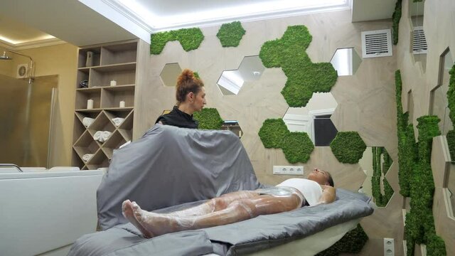 Young woman having body wrap skin treatment in spa salon from beautician for healthy skin