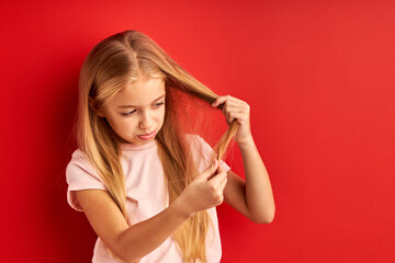 child girl examining her hair ends with sadness, check the split ends, want to cut, isolated on red background