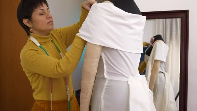 Seamstress sews wedding dress on mannequin