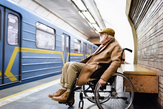 Elderly Handicapped Man In Wheelchair, Wearing Autumn Clothes, Near Train On Subway Platform