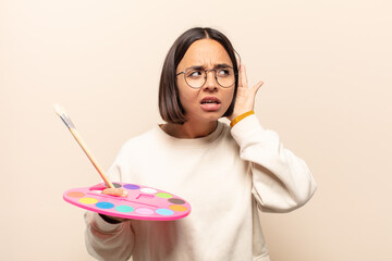 young hispanic woman looking serious and curious, listening, trying to hear a secret conversation...