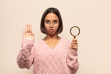 young hispanic woman looking serious, unhappy, angry and displeased forbidding entry or saying stop...