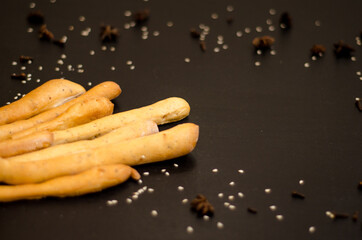 Ruddy grissini, dry long bread with sesame seeds, on a black background with spices, star anise and...