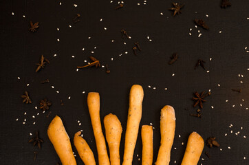 Ruddy grissini, dry long bread with sesame seeds, on black background with spices, star anise and...
