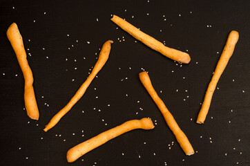 Ruddy grissini, dry long bread with sesame seeds, on black background with spices, star anise and...