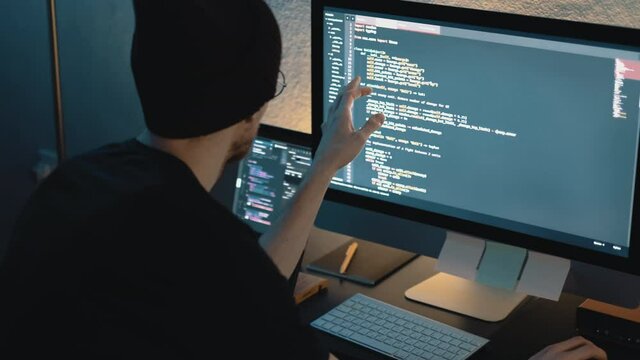 Young man mobile developer writes program code on a computer, programmer work in home office.