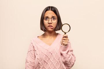 young hispanic woman looking puzzled and confused, biting lip with a nervous gesture, not knowing...