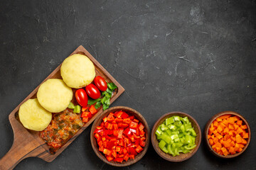Above view of uncooked vegetables on a cutting board and chopped foods on the black background
