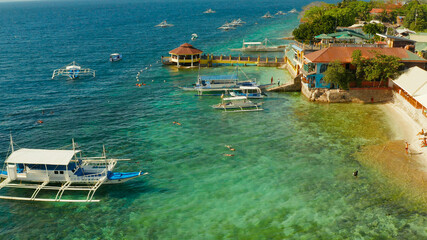 People snorkeling over coral reef with clear blue ocean water, top view. Moalboal, Philippines. People swim in the transparent sea between coral reefs. Summer and travel vacation concept.