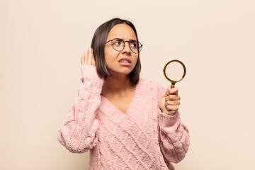 young hispanic woman looking serious and curious, listening, trying to hear a secret conversation...