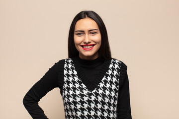 young hispanic woman smiling happily with a hand on hip and confident, positive, proud and friendly...