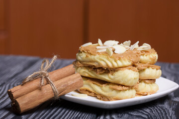 Eclairs cake smeared with cinnamon cream. Nearby ingredients for cooking. On black pine boards.