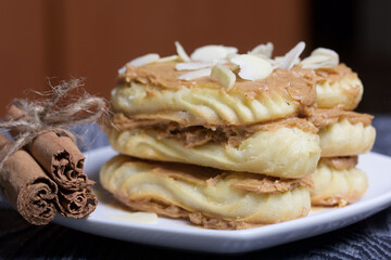 Eclairs cake smeared with cinnamon cream. Nearby ingredients for cooking. On black pine boards.