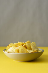 Crispy chips on a gray plate on a yellow table against a gray wall background, trendy colors of the year