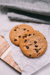 chocolate chip cookies on light background with linen napkins, a wooden cutting board, and baking paper. Yummy food background. Dessert image.
