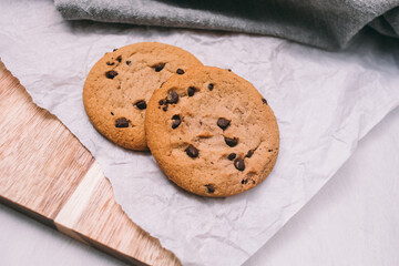 chocolate chip cookies on light background with linen napkins, a wooden cutting board, and baking paper. Yummy food background. Dessert image.