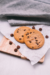 chocolate chip cookies on light background with linen napkins, a wooden cutting board, and baking paper. Yummy food background. Dessert image.
