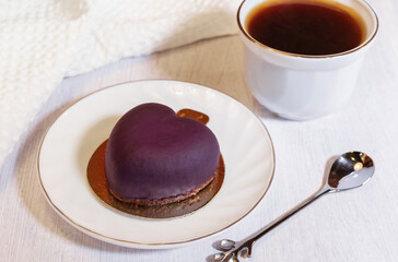 Purple tropical mousse cake decorated heart shape on plate a white background with cup of tea or coffee closeup view
