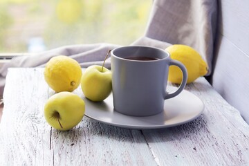Hot tea in a large cup, lemons and apples on a wooden table, yellow and gray color, vitamin drink concept, home comfort